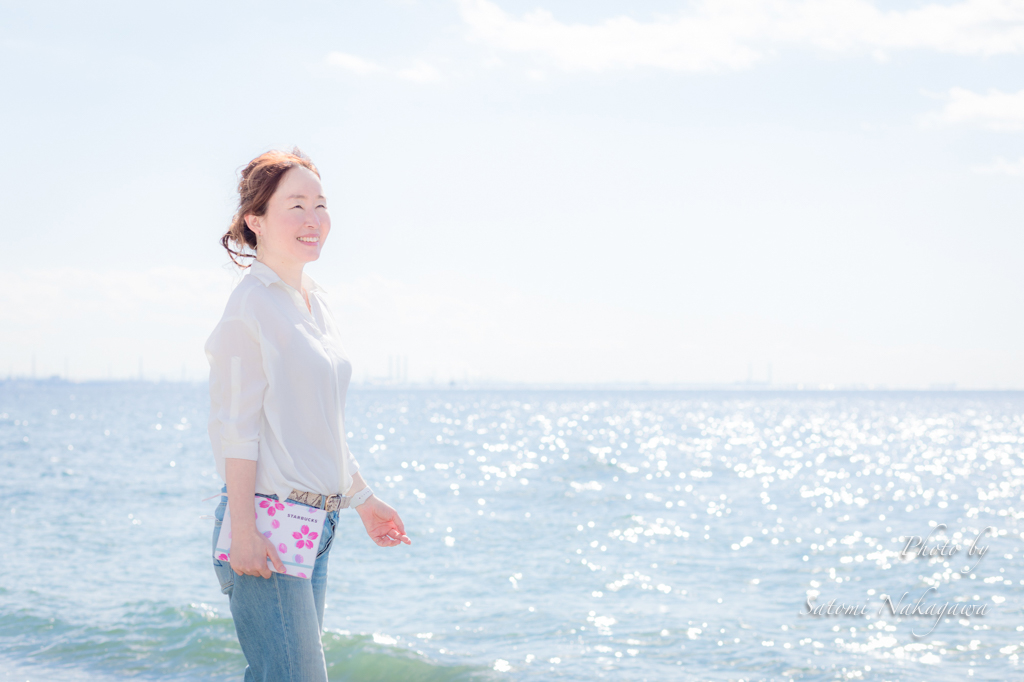 海をバックに手帳を持って笑顔の女性