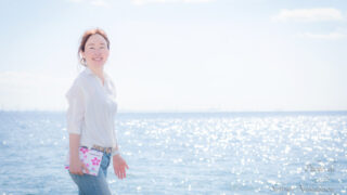 海をバックに手帳を持って笑顔の女性