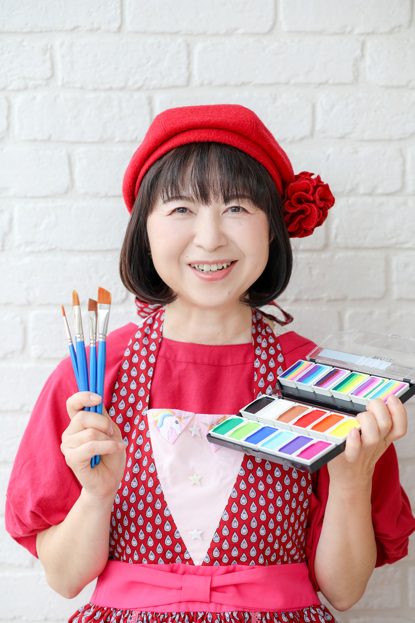 白い壁の前で絵の具を持って笑顔の女性