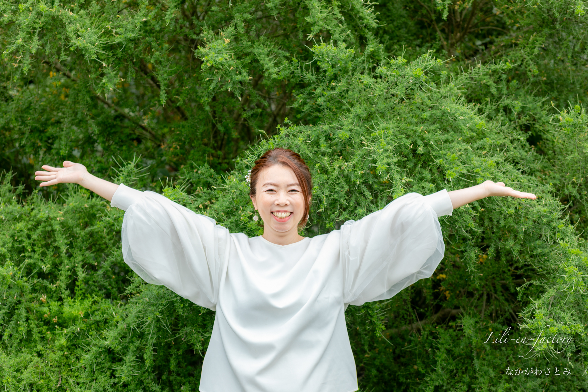 緑の前で手を大きく開いた笑顔の女性
