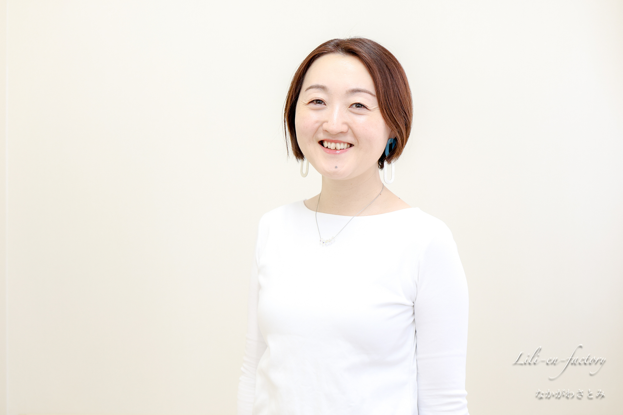 白壁の前で白い衣装で笑顔の女性